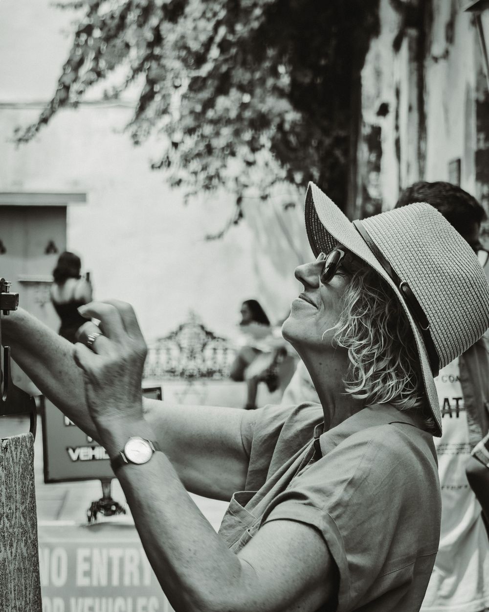 A black and white photo of someone in a bucket hat taking a picture with a vintage camera.