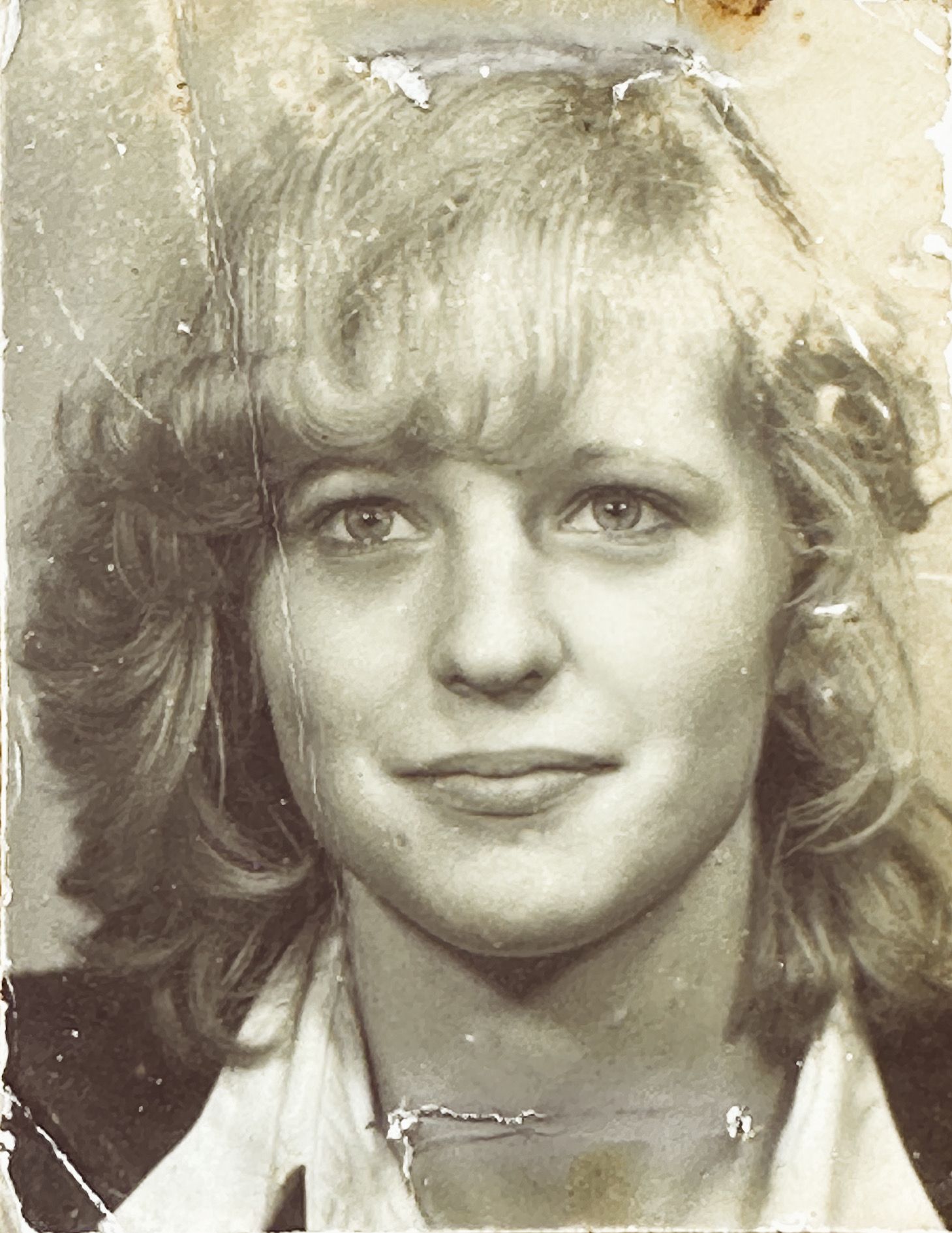 A vintage black and white photograph from the 1980s showing a young person with feathered hair and a slight smile.