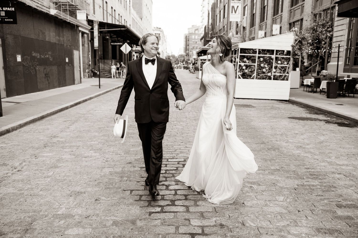 Black and white photo of newlyweds walking down a cobblestone street.