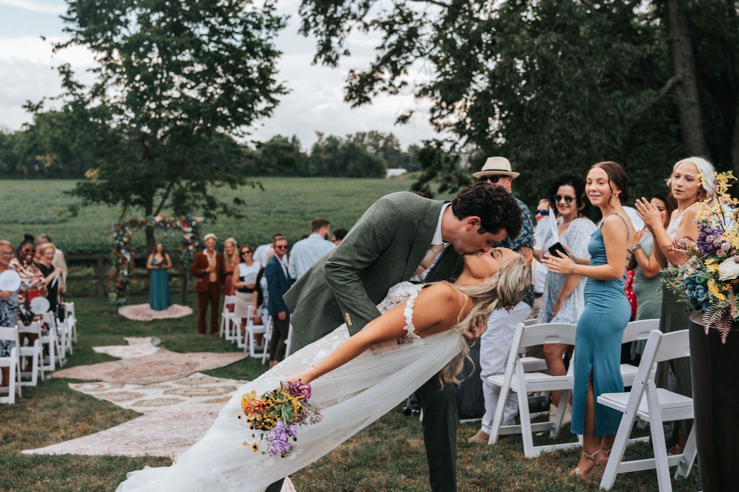 A couple holds hands during their outdoor wedding ceremony, with the bride wearing a delicate lace dress.