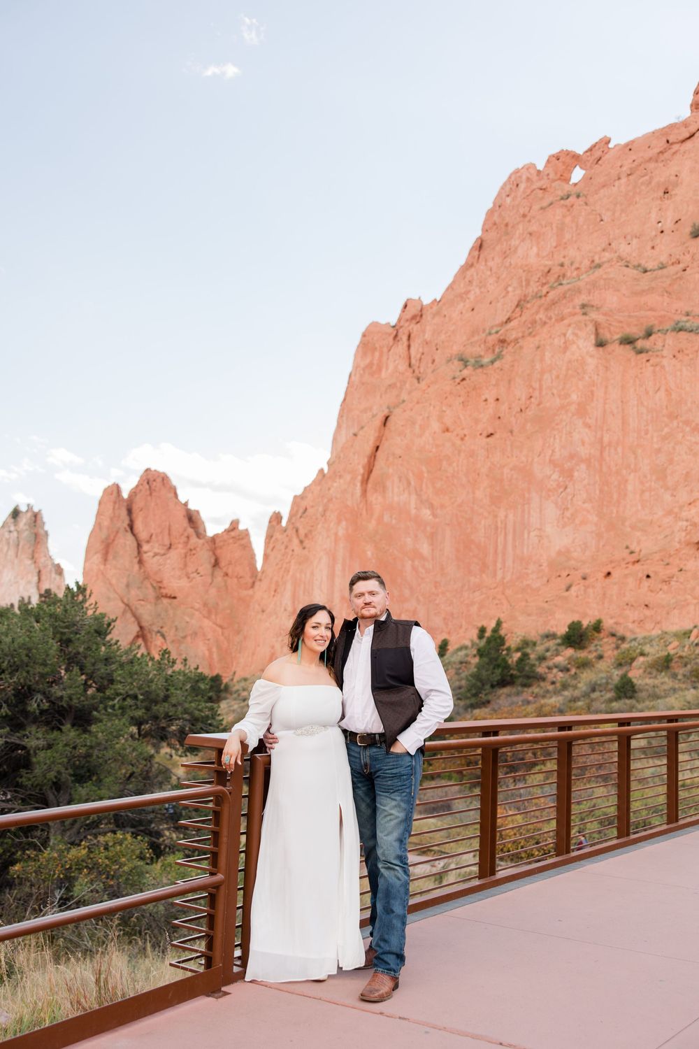 A couple poses together on a wooden walkway with stunning red rock formations of Garden of the Gods in the background.