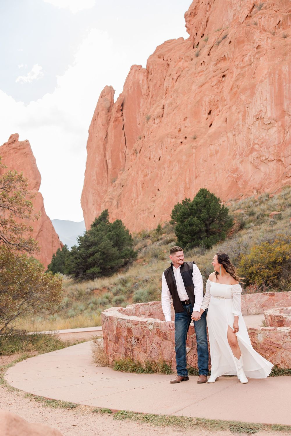 A romantic couple poses along a winding trail at Garden of the Gods with towering red rock formations in the background.