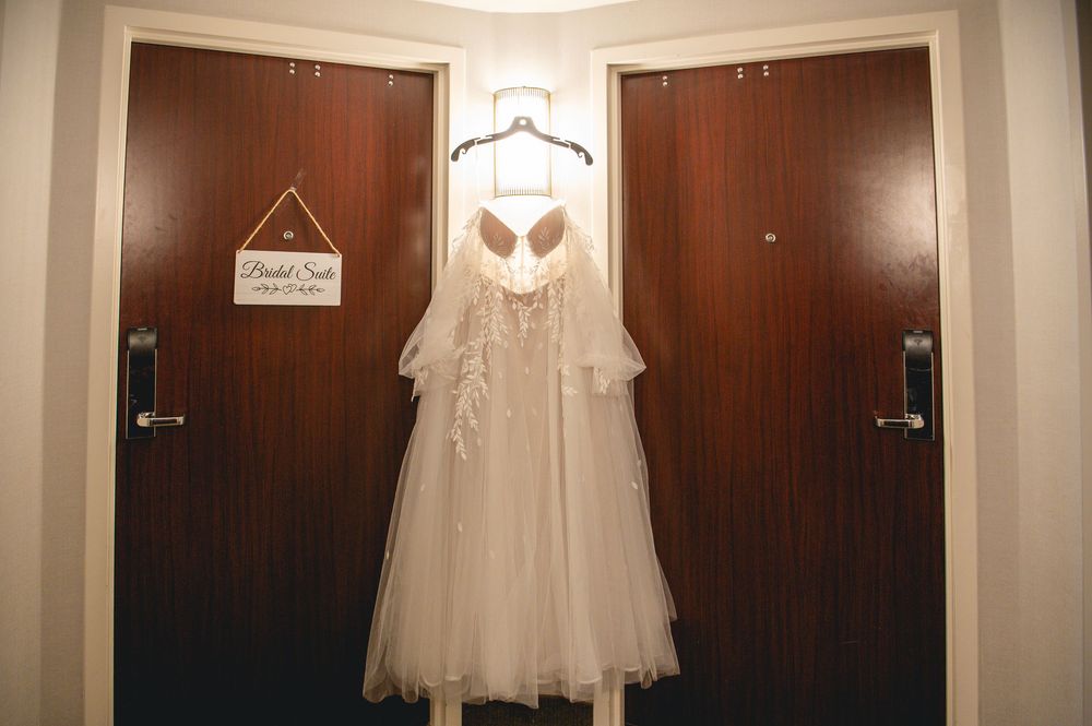 White wedding dress hanging in front of dark wooden doors in a dimly lit hallway.