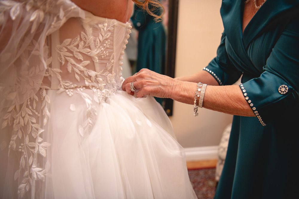 Close-up view of hands adjusting a white wedding dress with delicate lace details and beading.