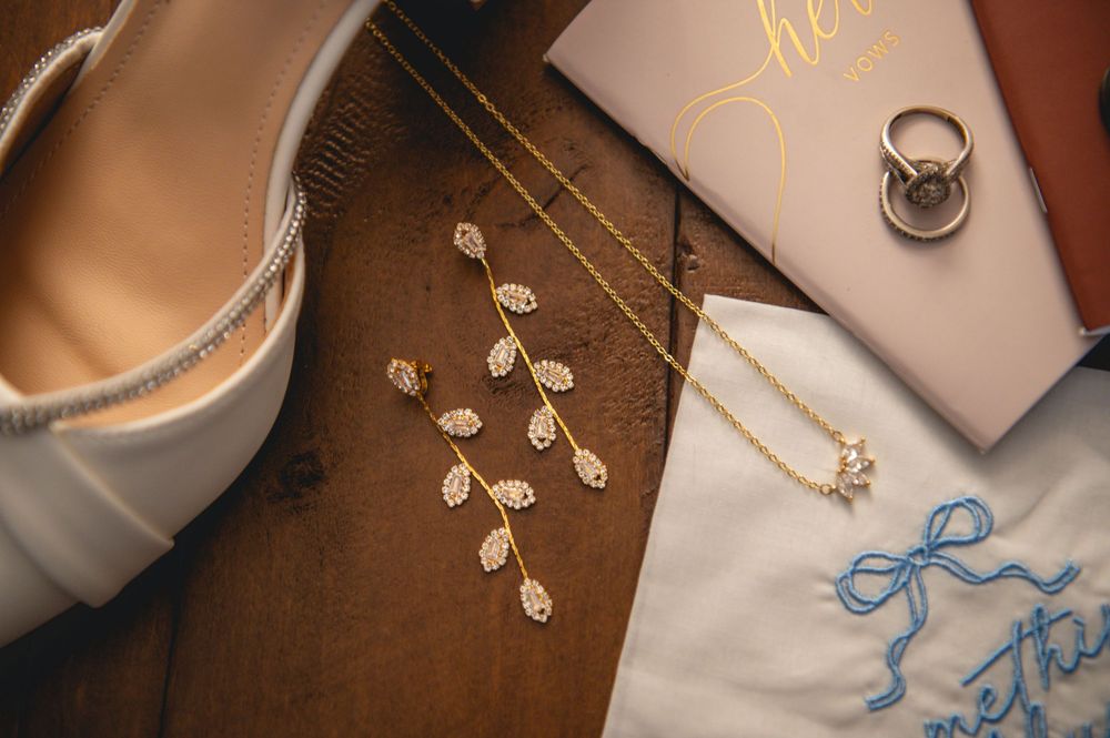 Wedding jewelry and accessories including delicate rings, floral hair pieces, and blue ribbon details laid out on brown surface.