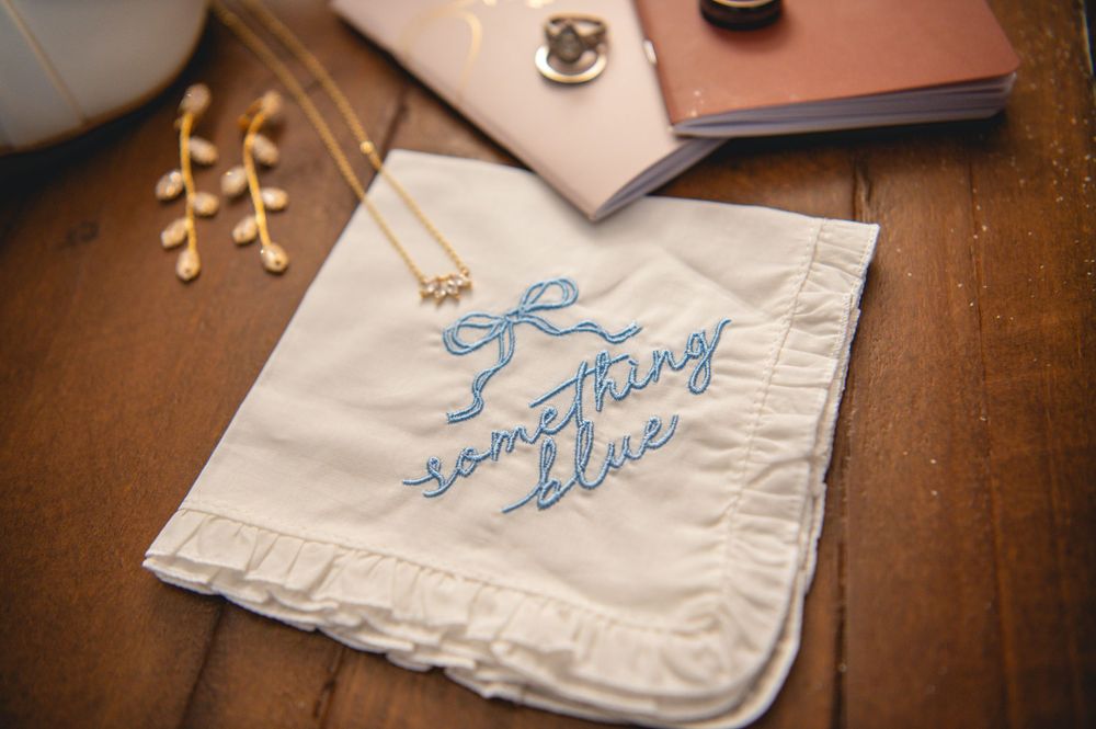 Embroidered handkerchief with blue stitching laid flat on a wooden surface.