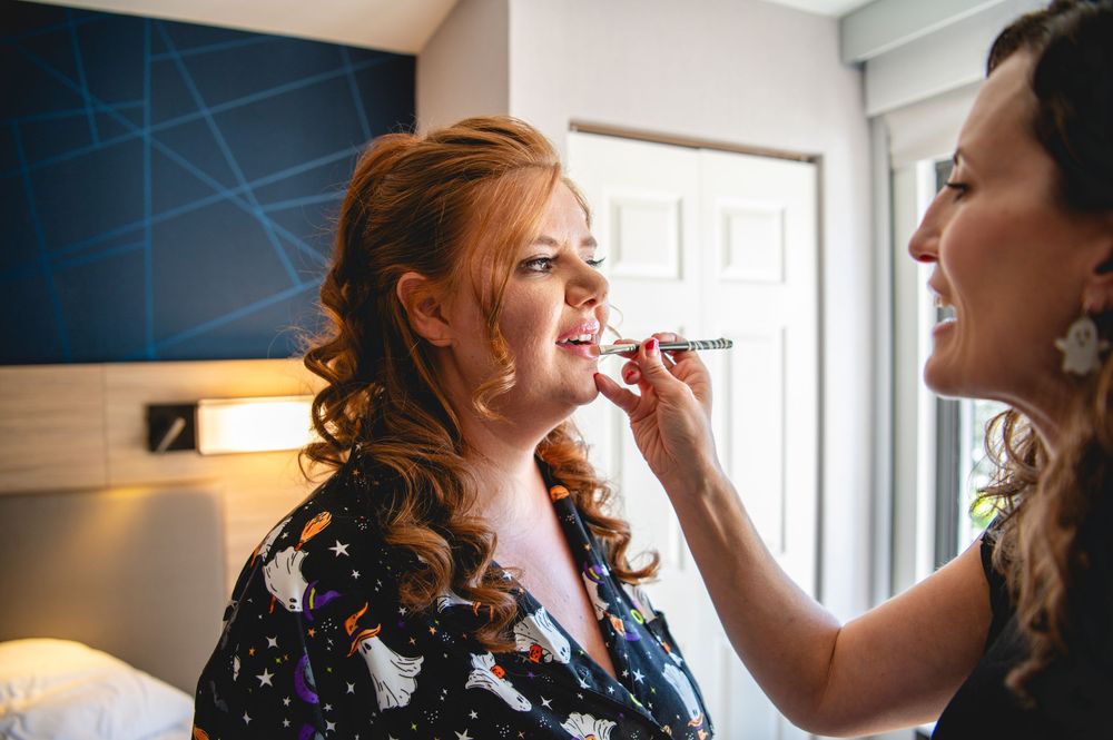 Makeup artist applies cosmetics on a client in a bright, naturally lit room during a beauty preparation session.