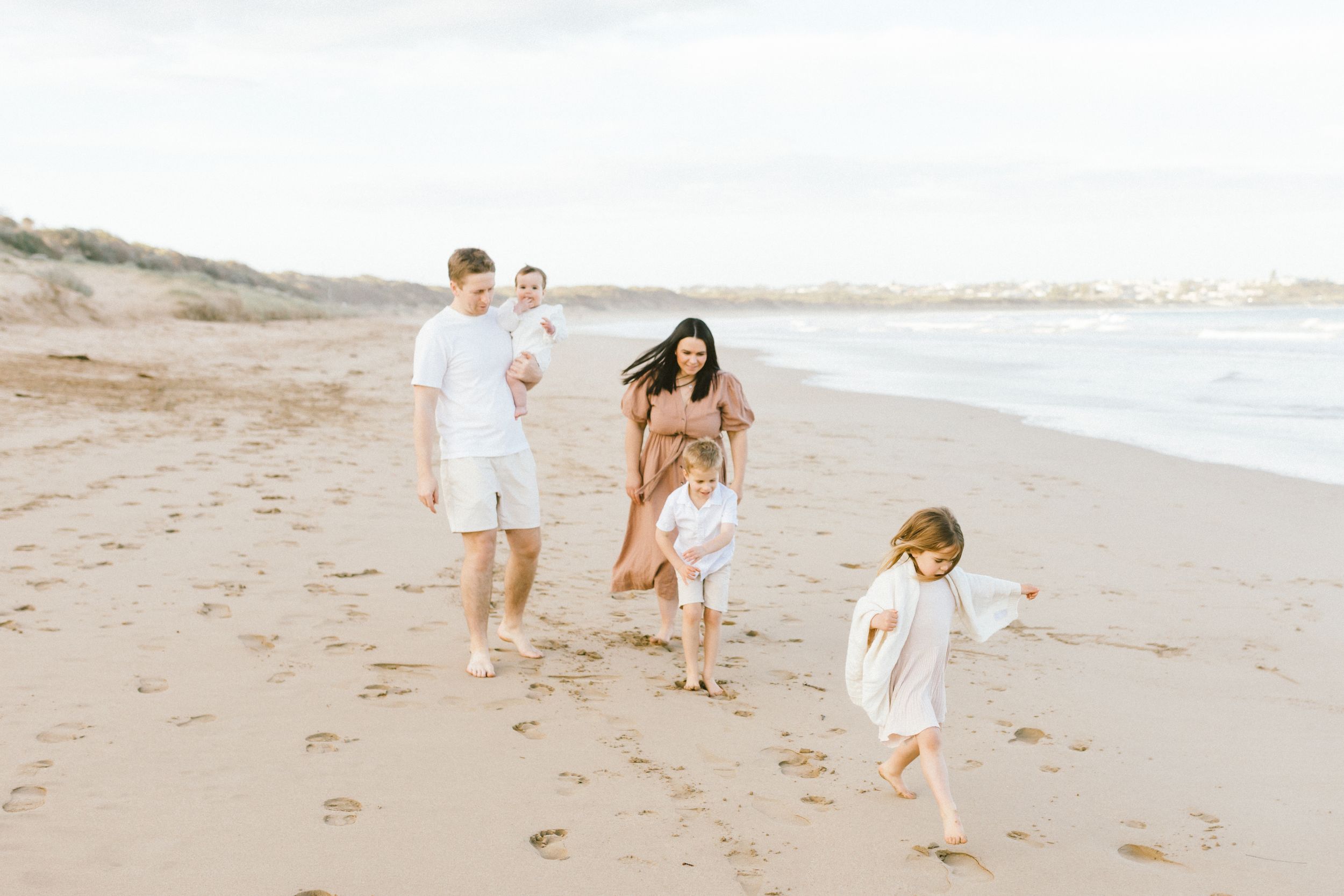 A family enjoys a peaceful walk together along a sandy beach during golden hour.