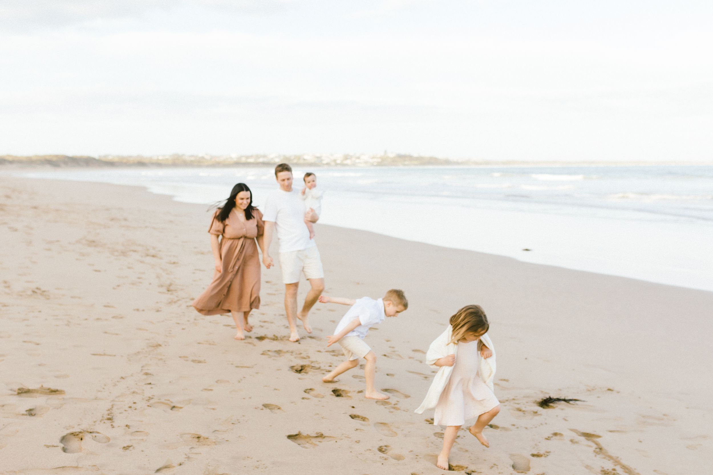 A family walks together along a sandy beach at sunset with ocean waves in the background.