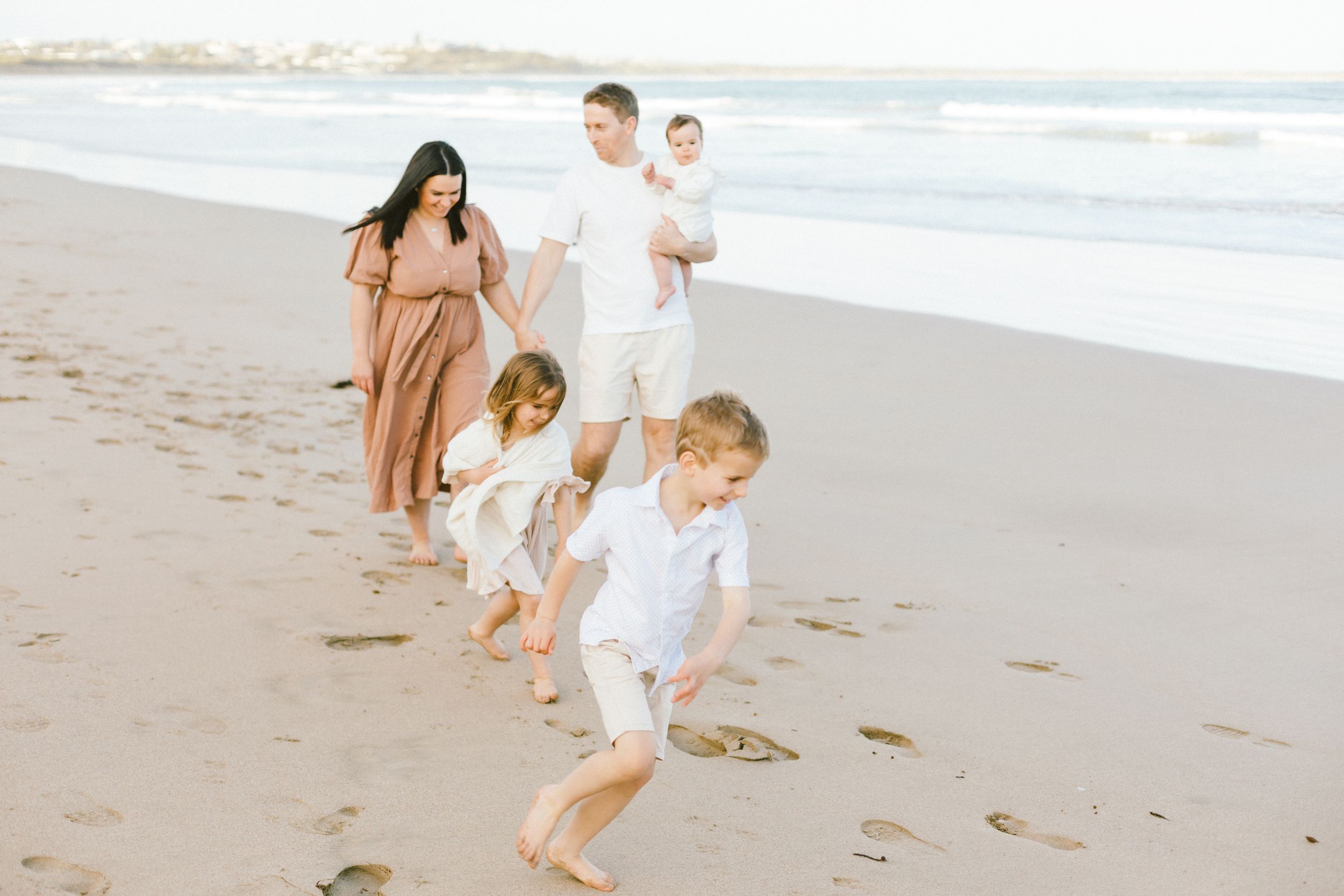 Group in coordinated white and tan outfits strolling on a peaceful beach at sunset.