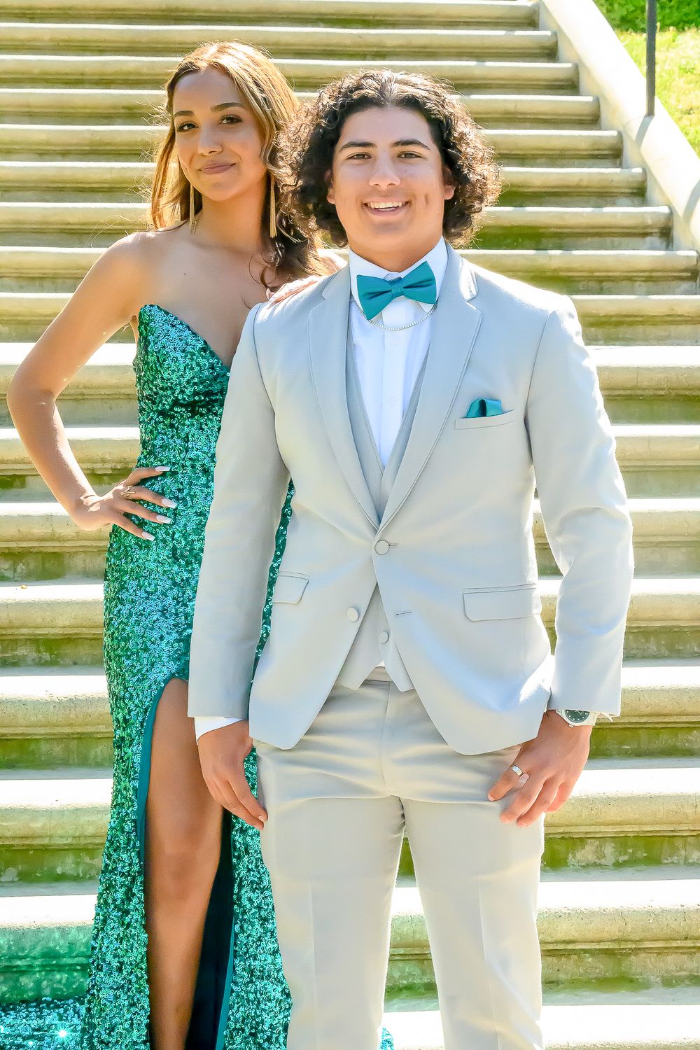 Formal group photo on stone steps with people wearing green sequin dresses and light gray suits with bow ties.