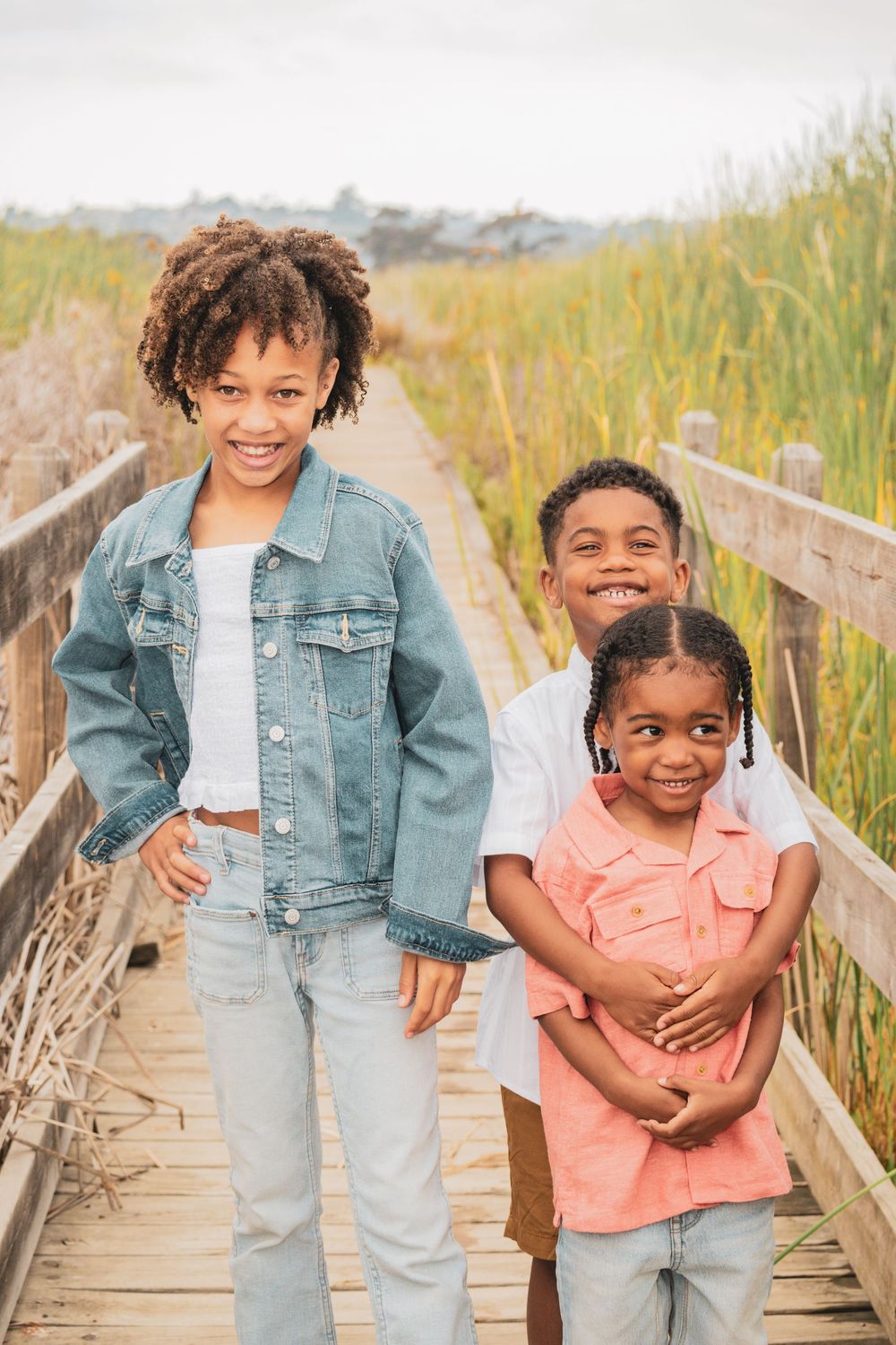 A family shares joyful moments together while walking on a wooden boardwalk surrounded by marsh grass.