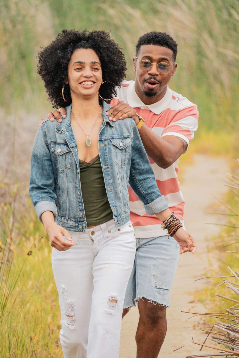 A couple walks through tall grass on a sunny day wearing casual summer outfits and denim.