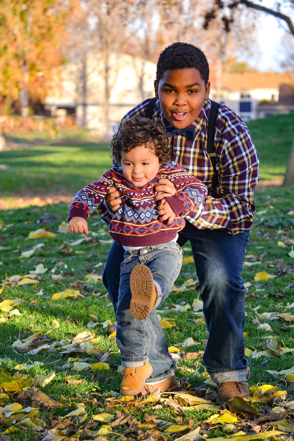 Playful autumn scene with people in matching sweaters playing in fallen leaves on a sunny day.