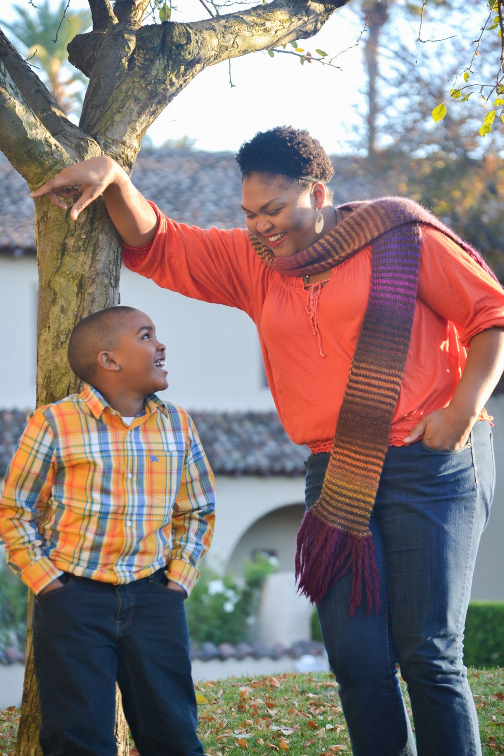 Joyful interaction between two people playing and laughing together under a tree in casual attire.