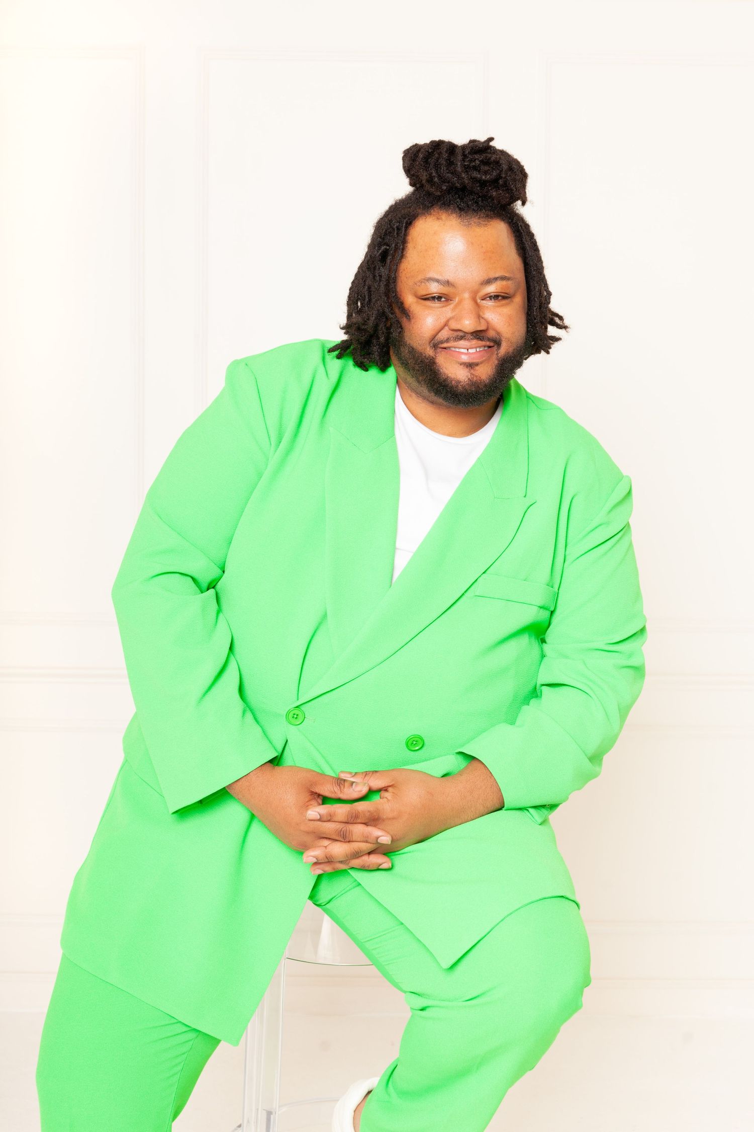 Portrait of person in bright lime green suit sitting casually against white background.