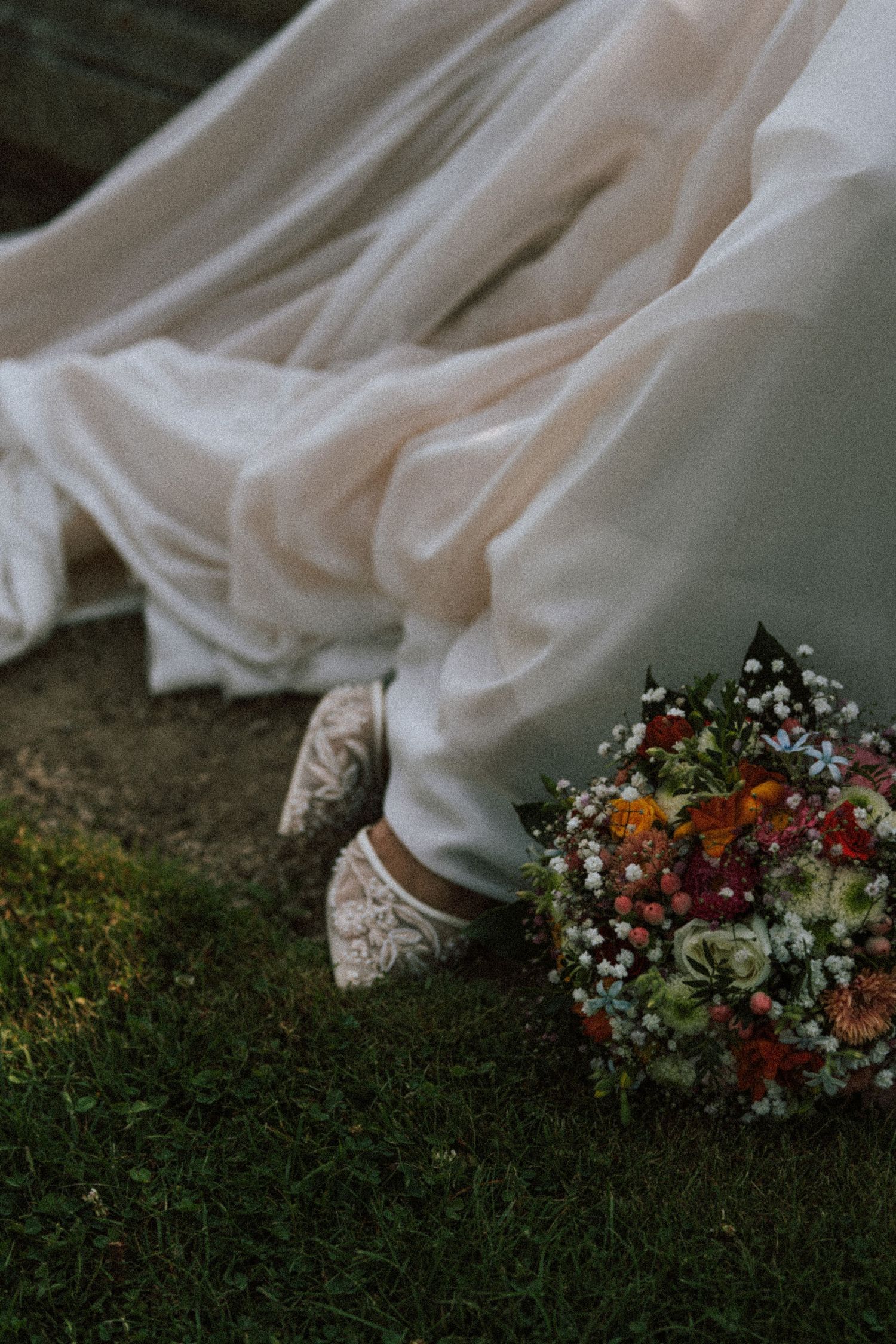 White wedding dress hem with sneakers and colorful floral bouquet on grass.