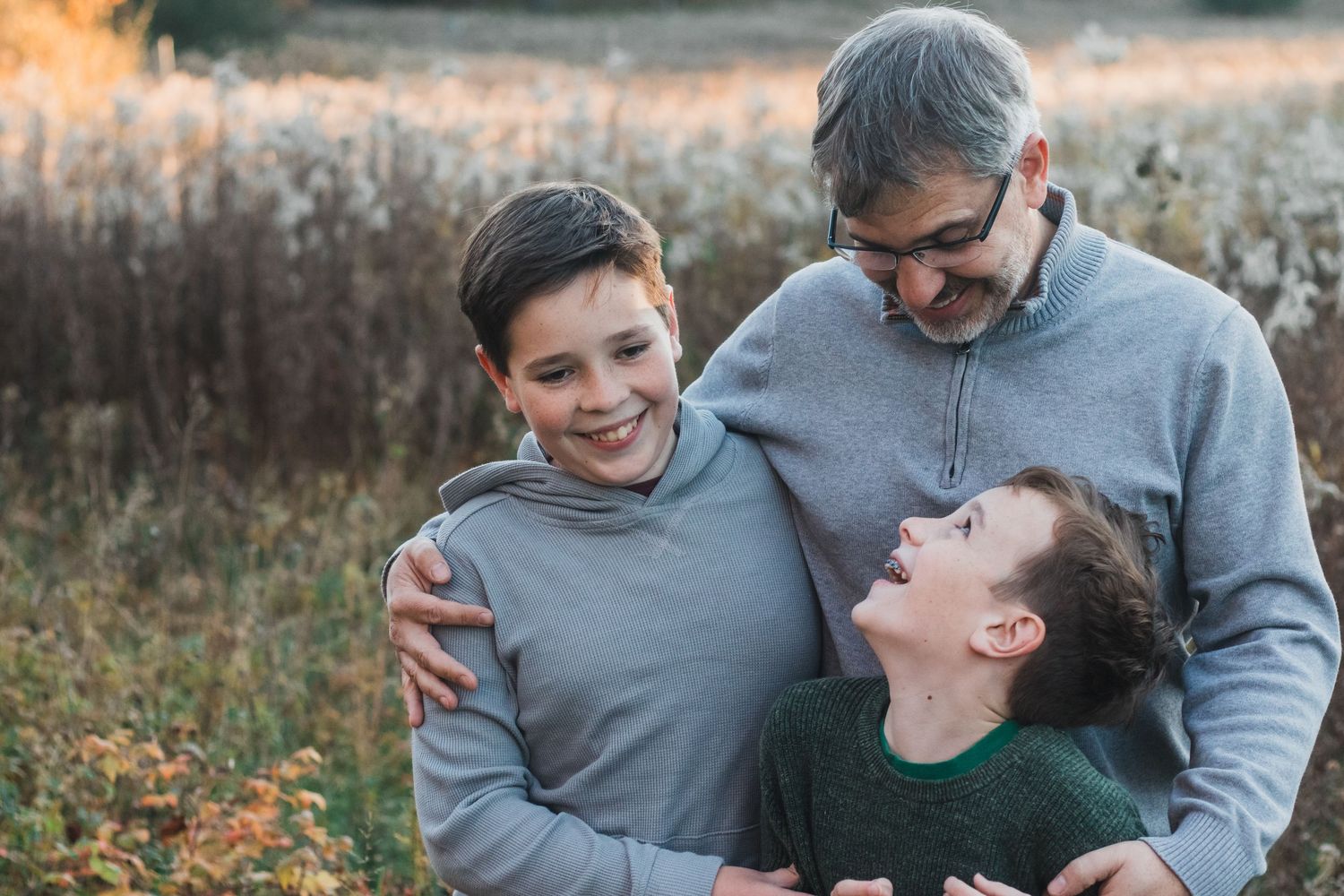 Father with two young boys smiling and embracing in an autumn field.