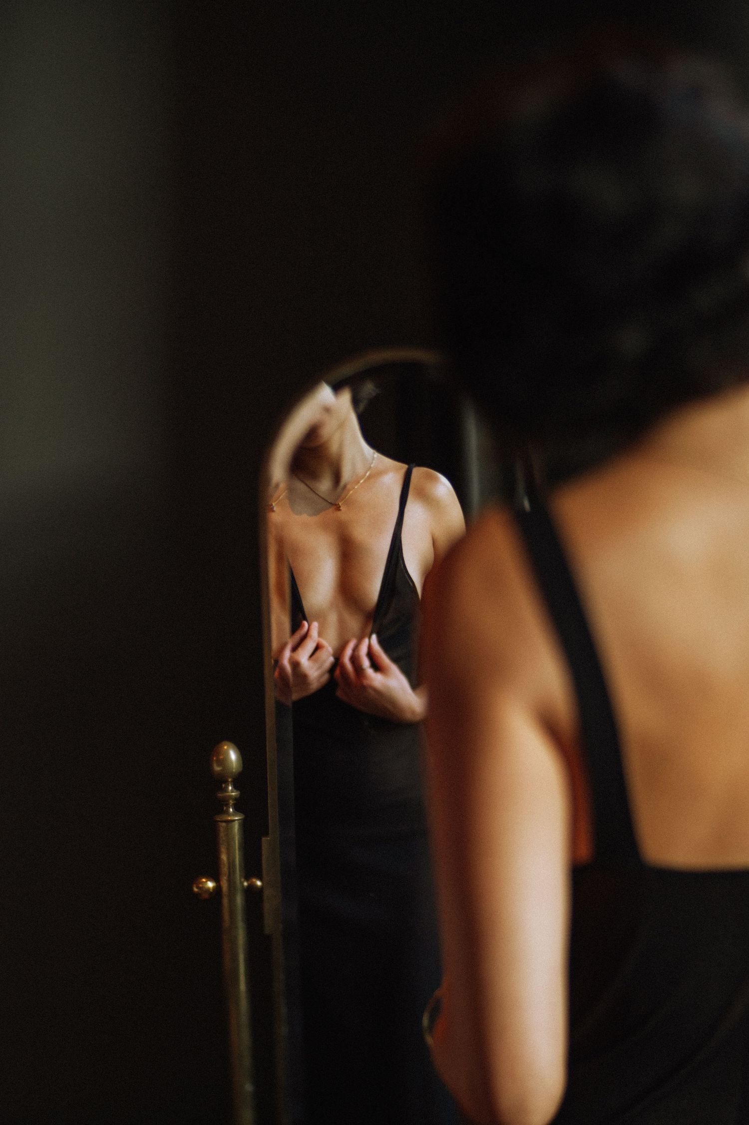 Woman in black dress adjusting her outfit in front of a mirror, intimate boudoir atmosphere, Amsterdam studio.