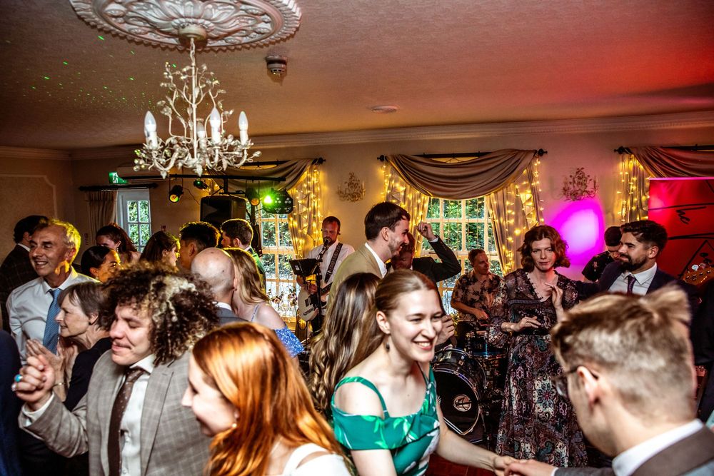 Wedding reception guests dance and celebrate in warmly lit elegant venue with chandelier and fairy lights.