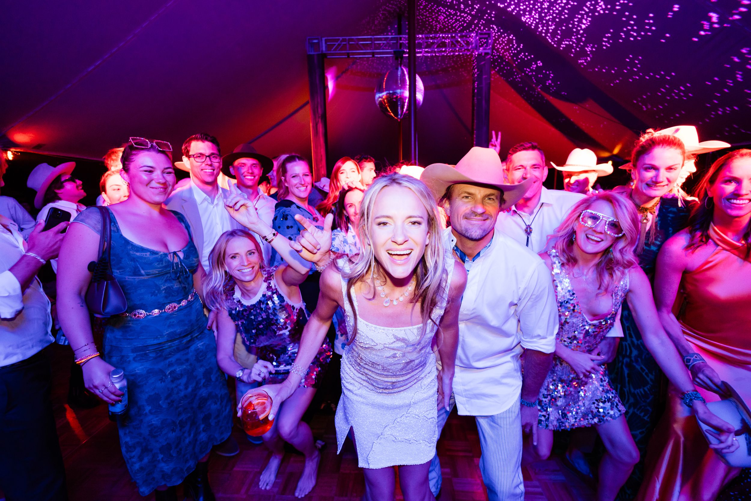 People dancing and celebrating together at a nightclub with vibrant purple and red lighting.