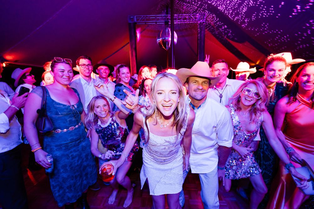 People dancing and celebrating together at a nightclub with vibrant purple and red lighting.