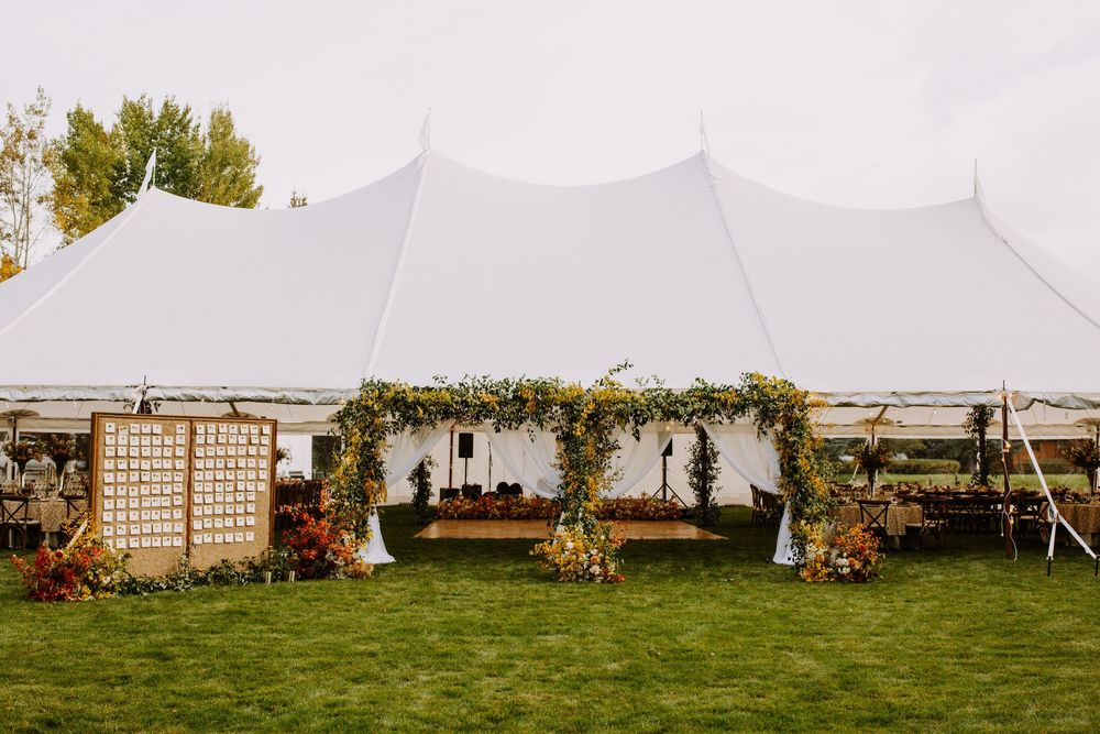 White wedding tent set up in a grassy field with lattice screens and floral arrangements for an outdoor celebration.