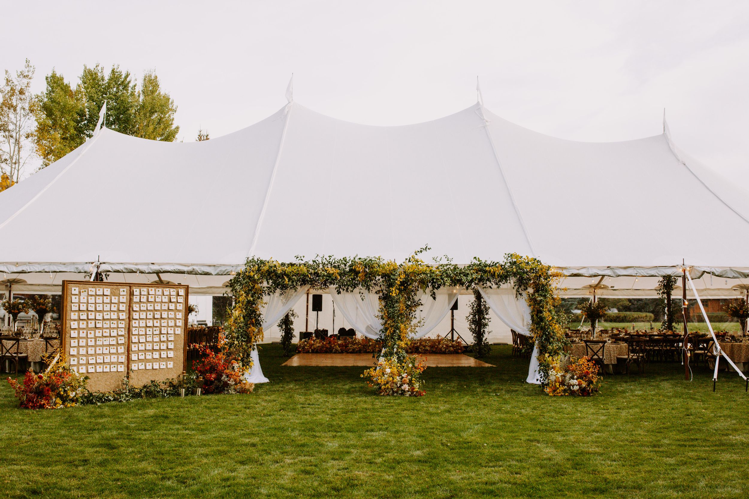 White wedding tent set up in a grassy field with lattice screens and floral arrangements for an outdoor celebration.