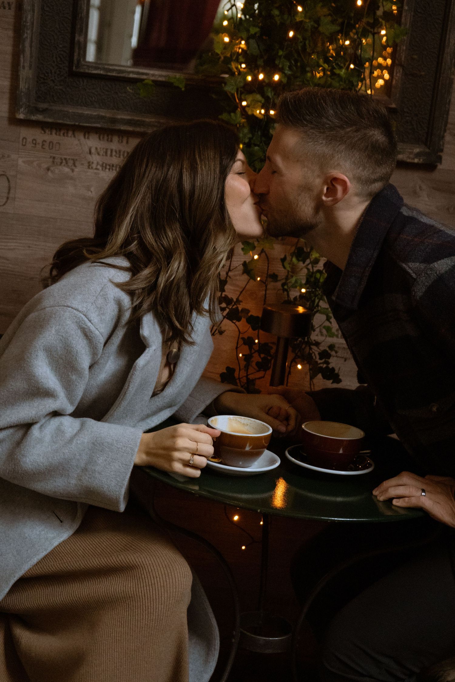 Cozy coffee date scene with warm lighting and Christmas decorations in background.