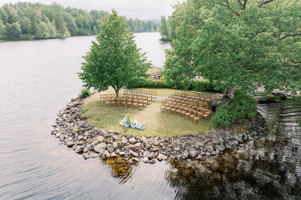 A panoramic view of a lake shoreline with trees, rocks, and wooden fencing along multiple connected segments.