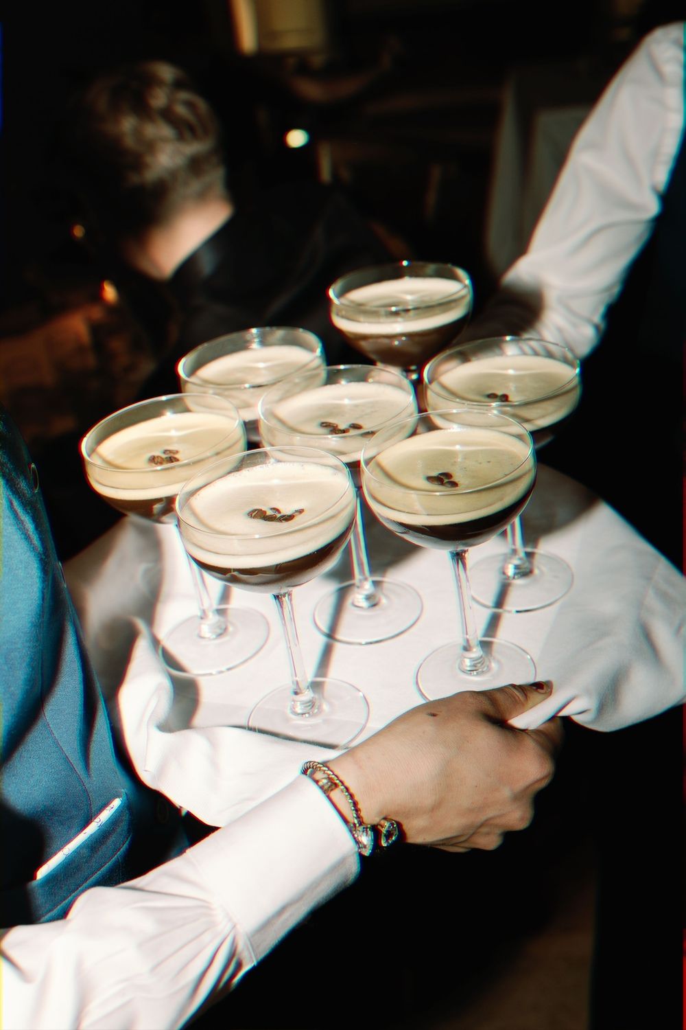 Server carrying multiple champagne cocktails on a white serving tray at an elegant event.