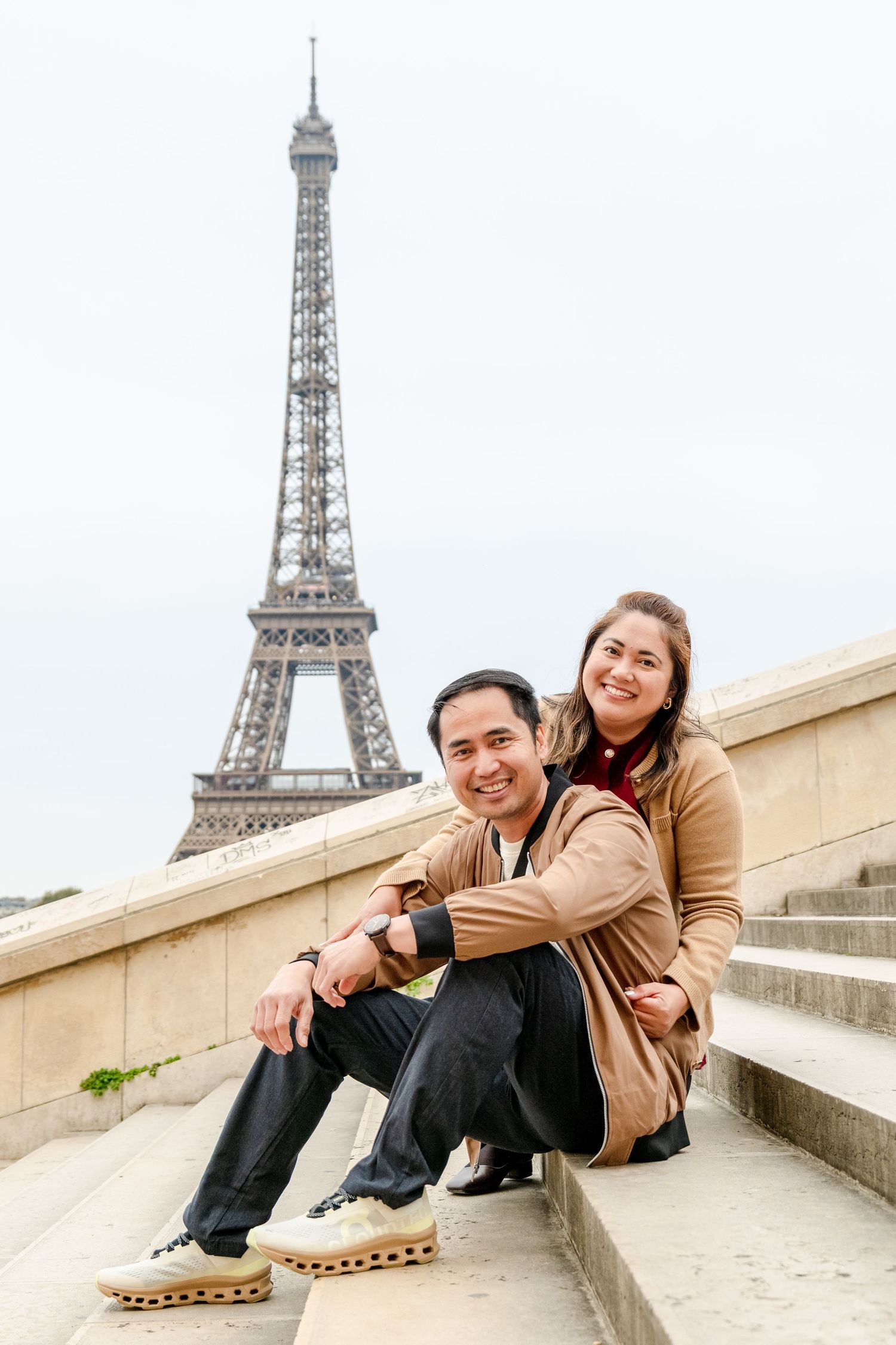 A couple sits and poses together on stone steps near the Eiffel Tower in Paris, shown in a series of candid moments.