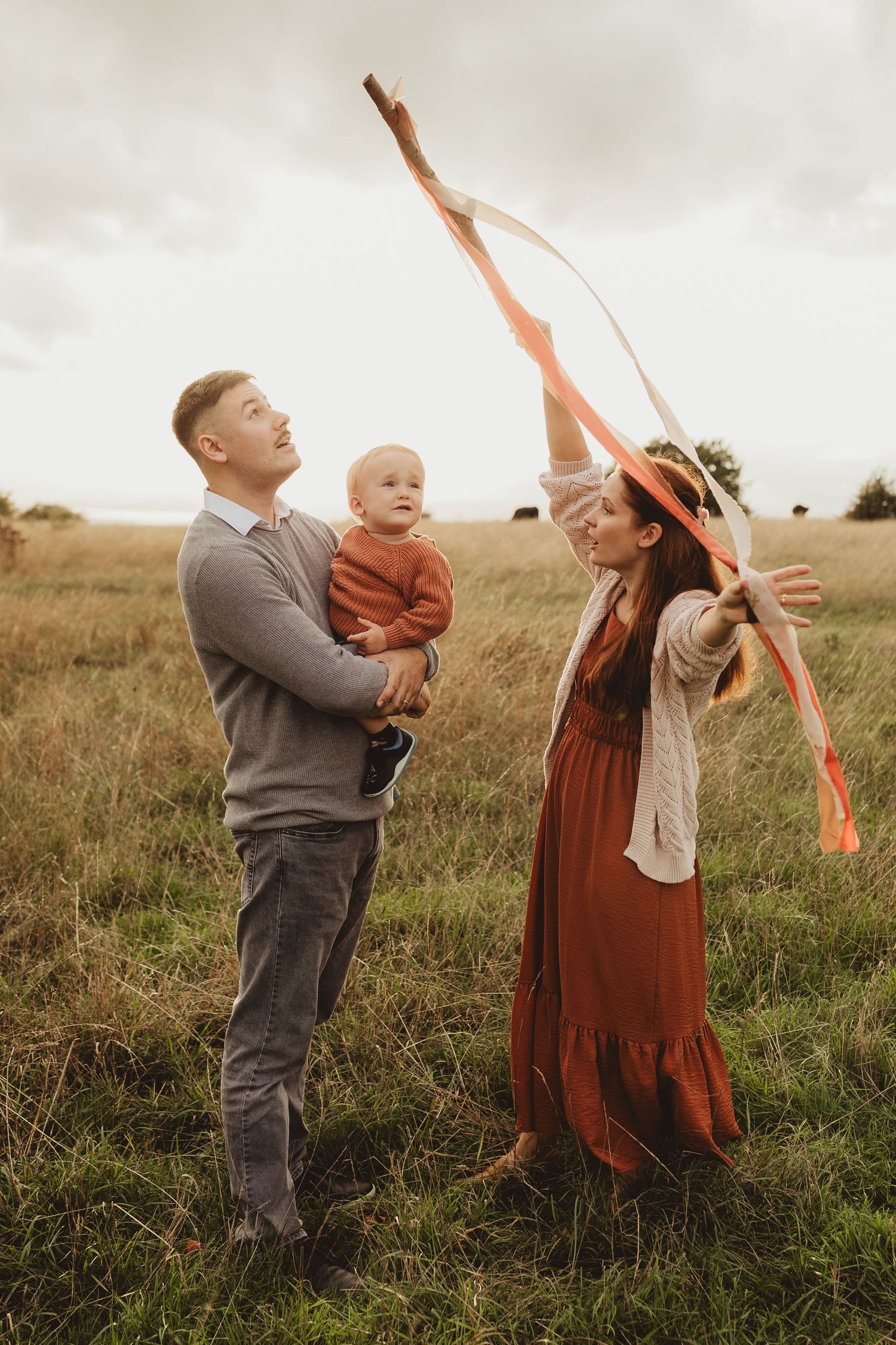 Family plays together with a flowing orange ribbon in a golden autumn field at sunset.