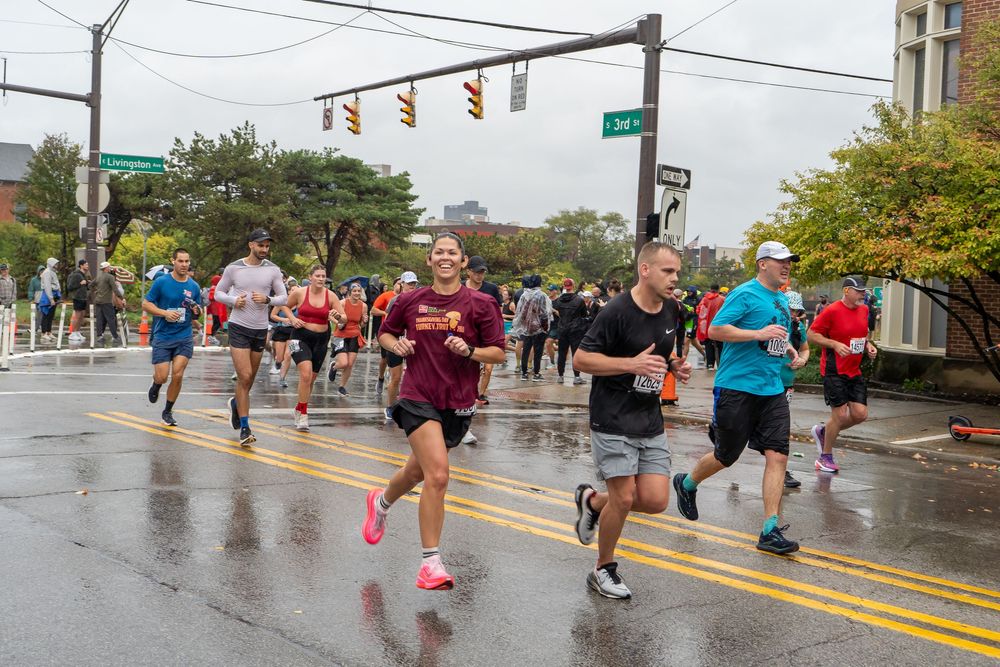 Runners compete in a rainy marathon on a wet city street with traffic lights visible in the background.