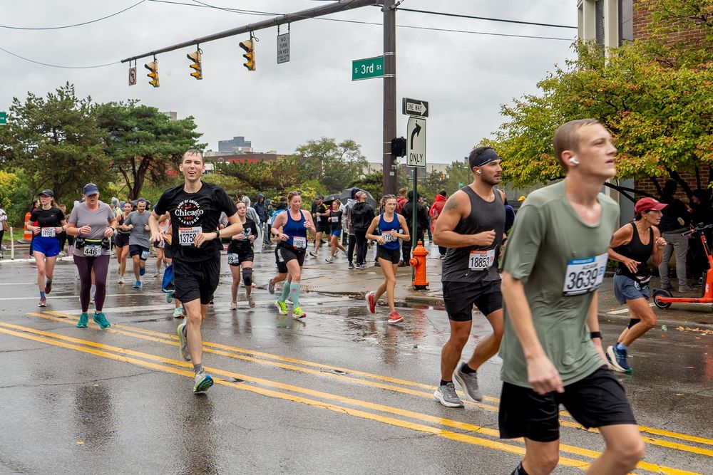 Marathon runners compete in a rainy urban race as spectators line the wet streets to cheer them on.