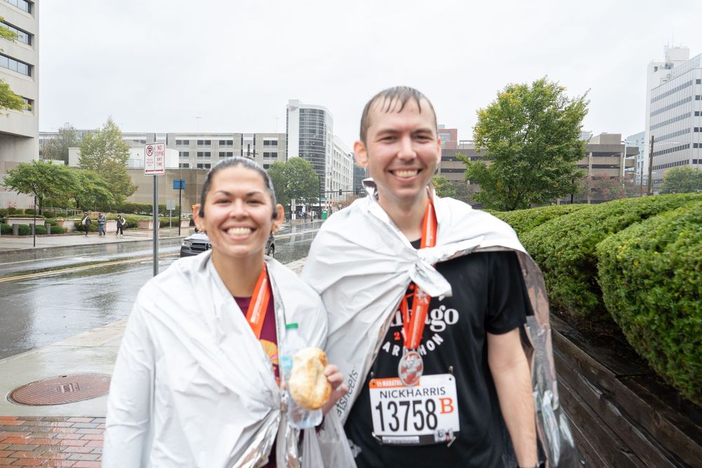 Runners celebrate together after completing a race in an urban setting on a cloudy day.