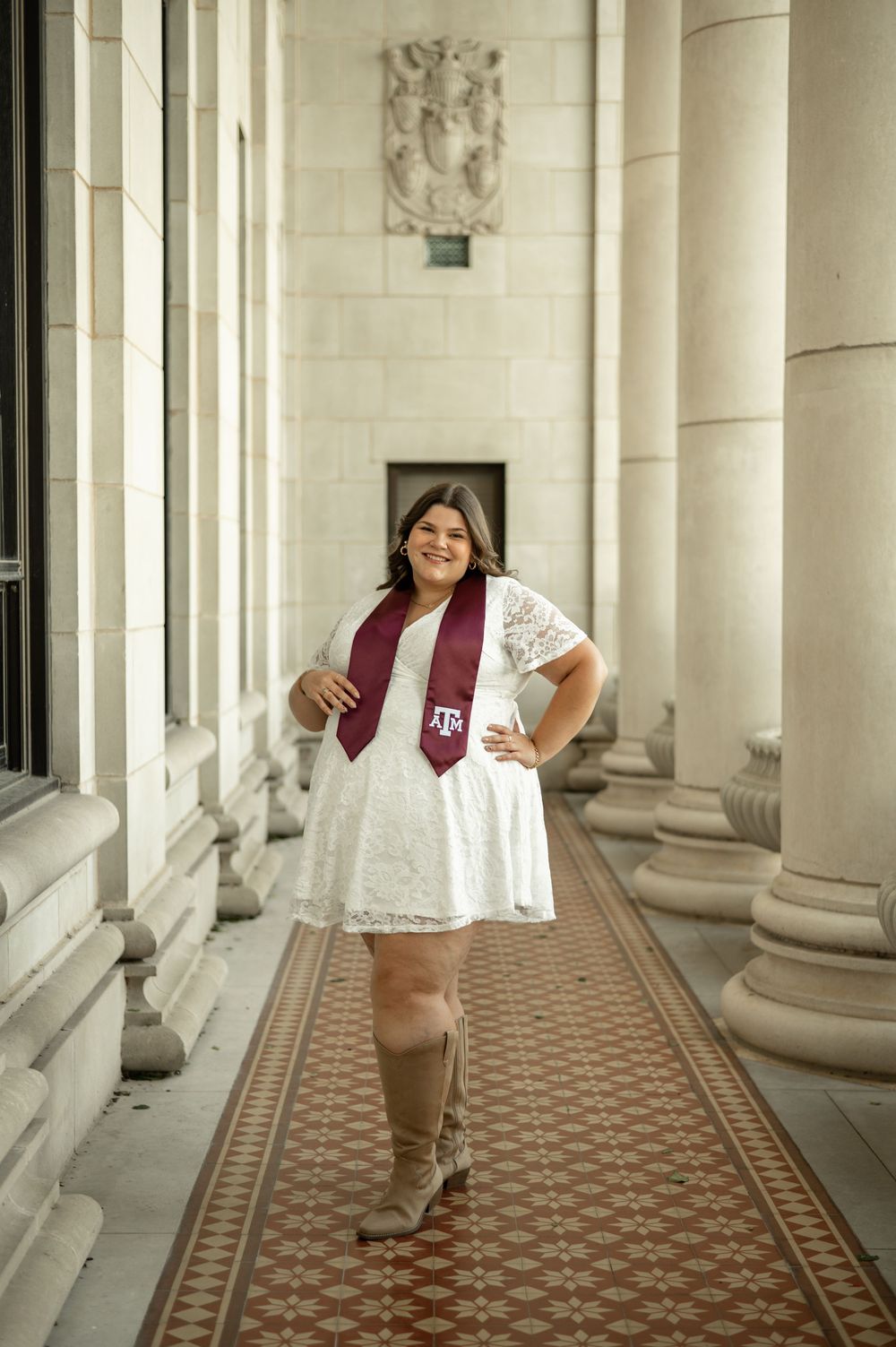 A college graduate poses between white columns wearing a maroon and white outfit during graduation photos.