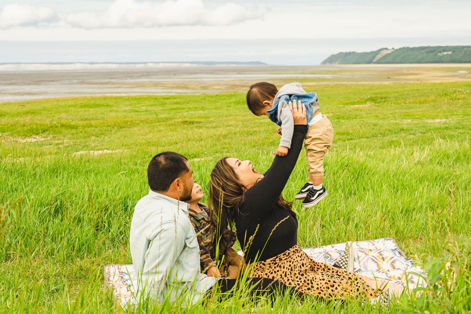 Family enjoying a picnic on a grassy meadow near the coastline on a bright summer day.
