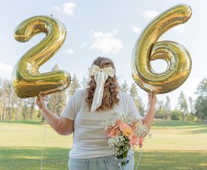 Gold number balloons spelling out 2023 being held up in a sunny park setting.