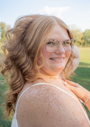 Outdoor portrait showing curled hair and glasses against a sunny natural background.
