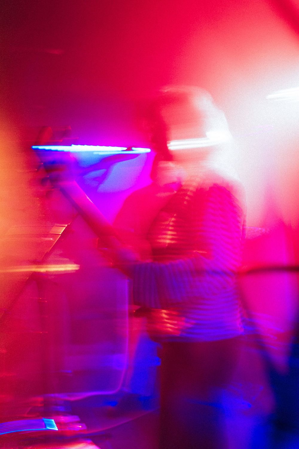 Abstract motion-blurred image of a drummer performing under vibrant red and blue stage lights at a live concert.