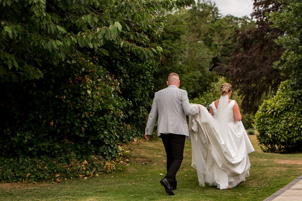 A couple walks hand in hand through a lush garden path on their wedding day.