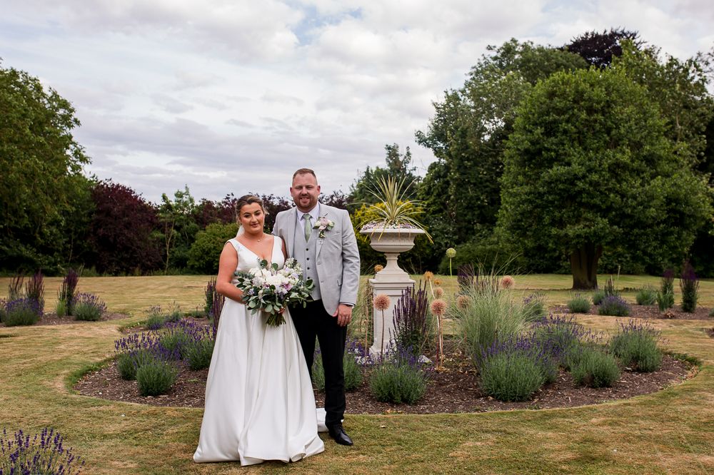 A wedding couple poses in a garden with lavender plants and greenery.