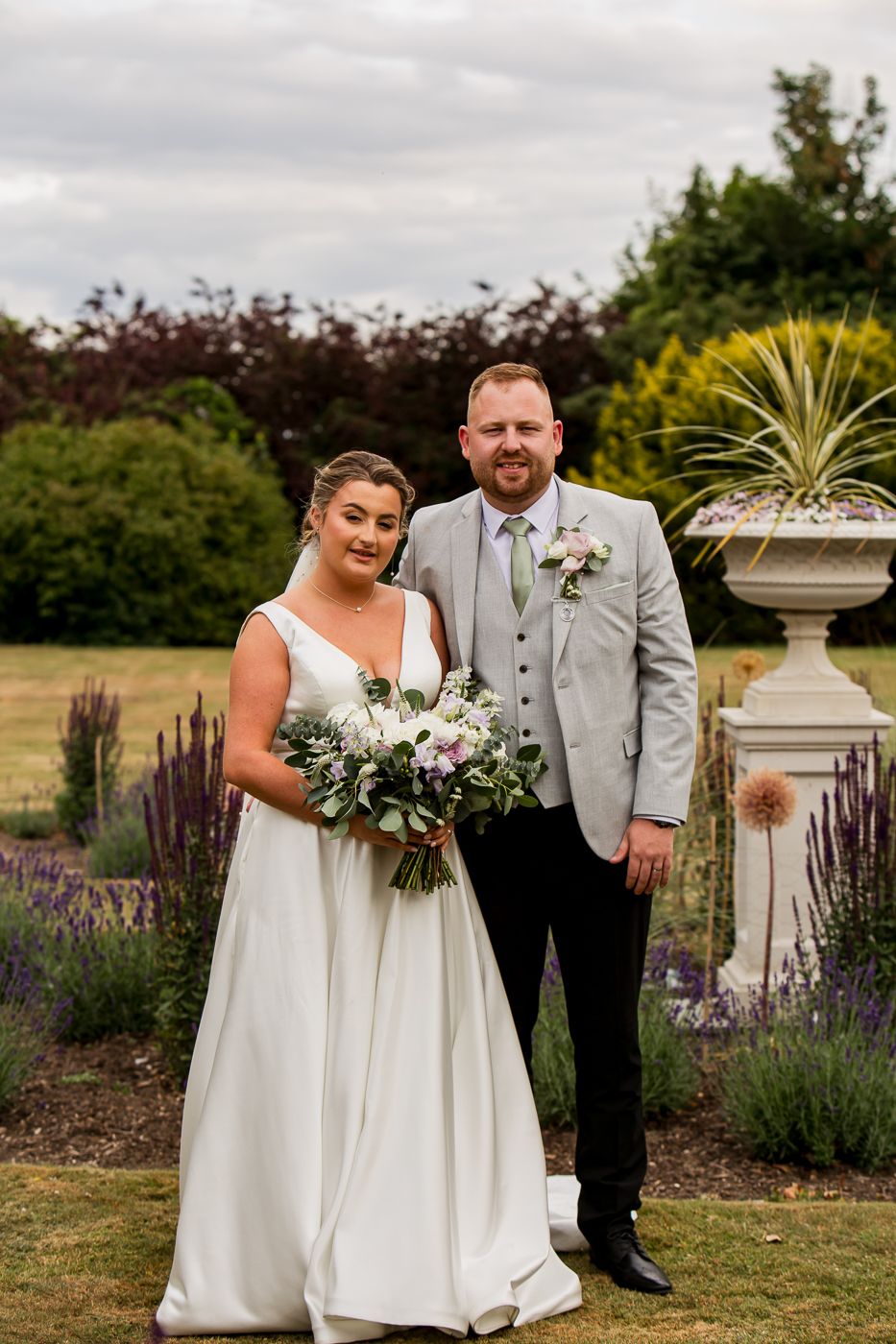 A wedding couple shares a joyful moment in a garden with blooming lavender and stone features.