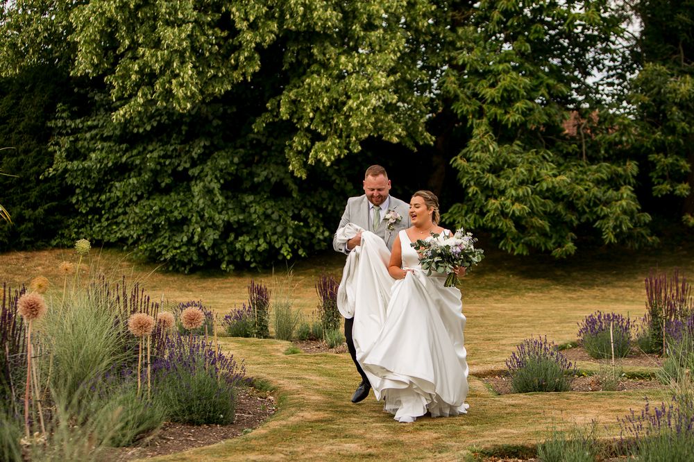 A wedding couple walks together through a garden landscape with blooming flowers.