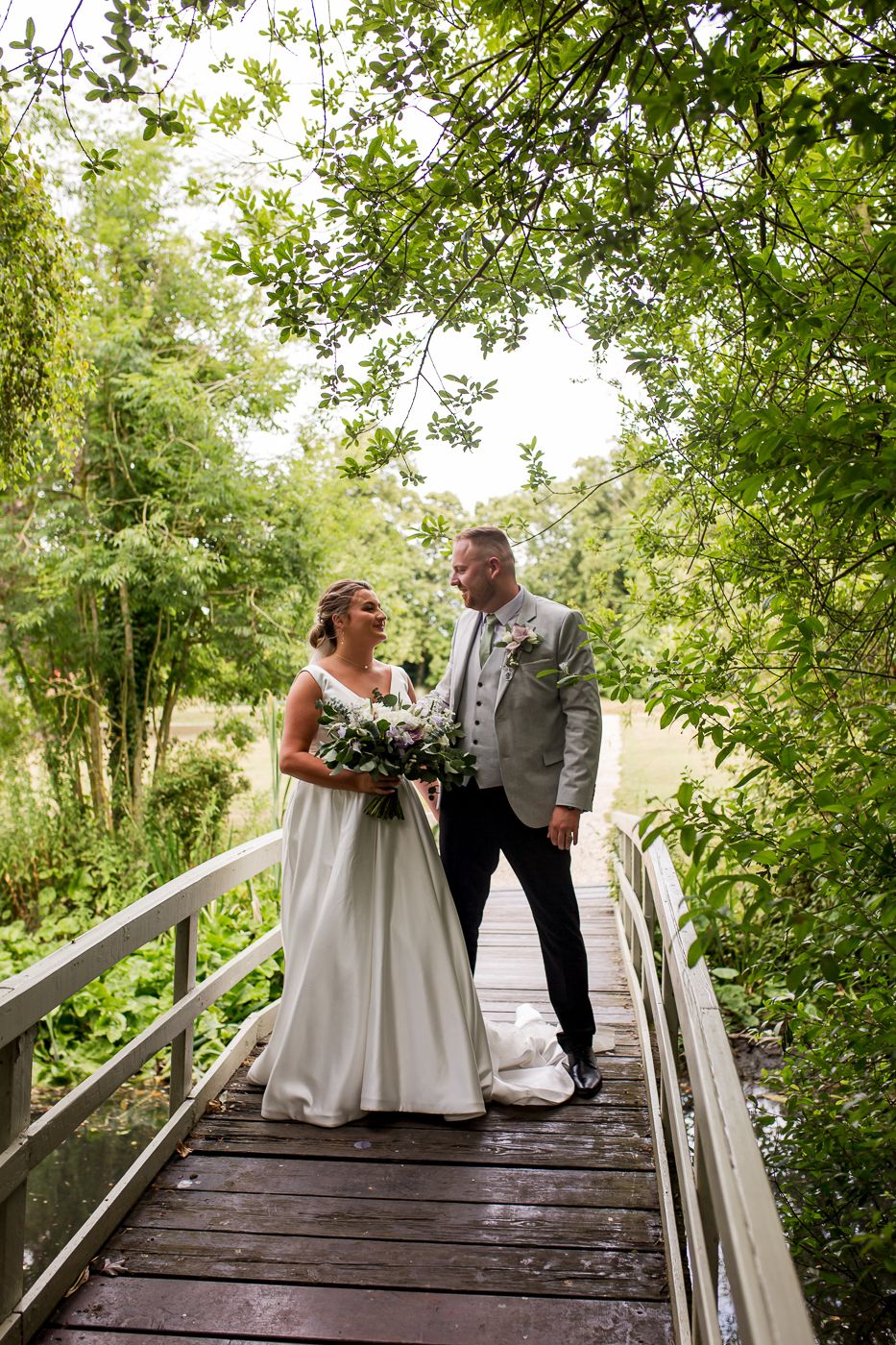 A couple shares intimate moments on a rustic wooden bridge surrounded by green foliage.