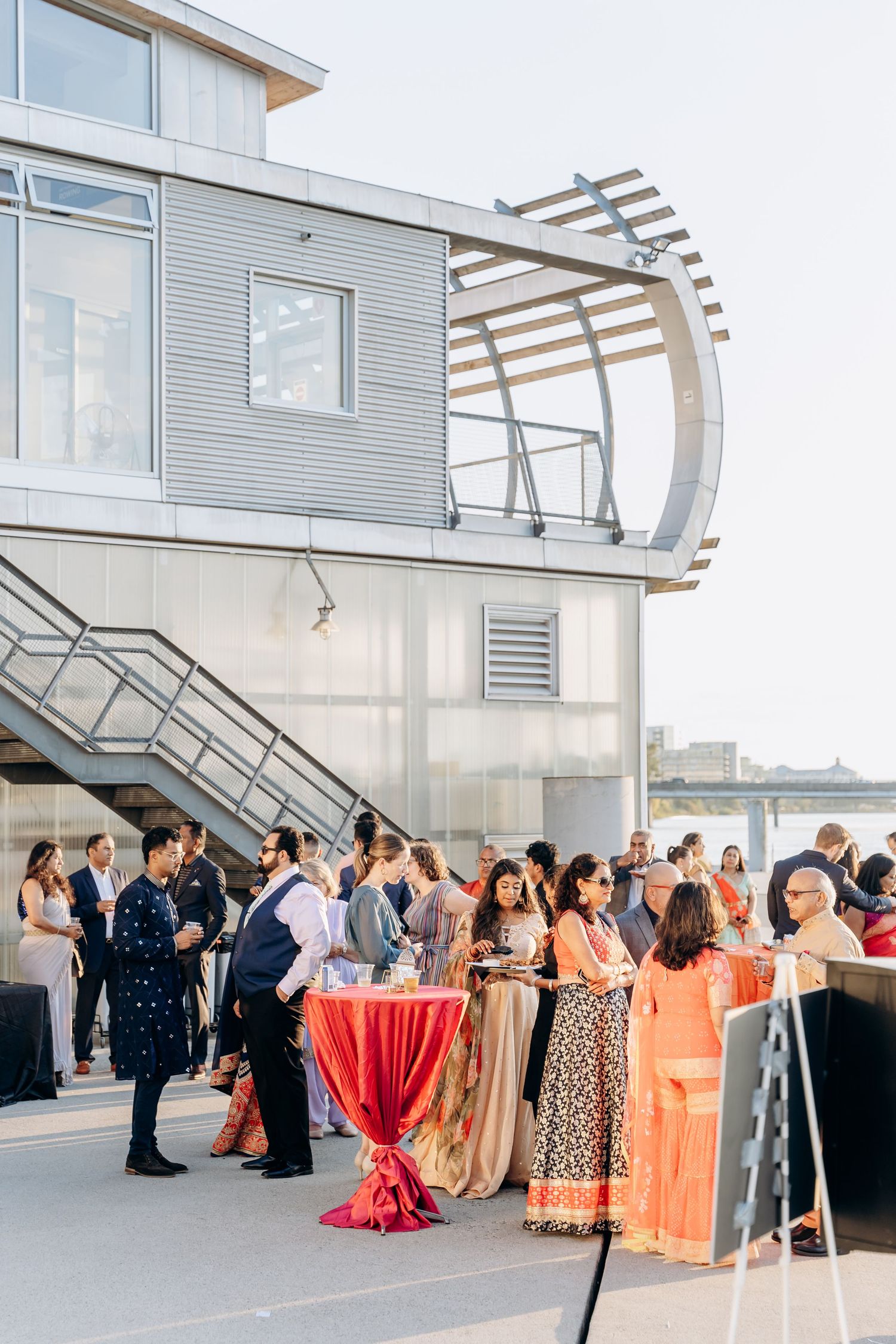Guests mingle at an elegant outdoor reception on a modern waterfront venue with curved architectural details.