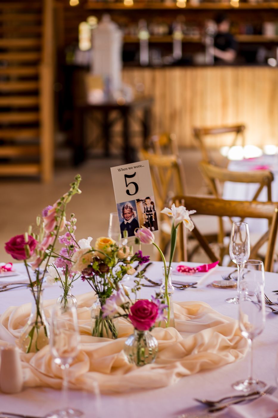 Wedding table centerpiece featuring delicate flowers in bud vases with table number five.