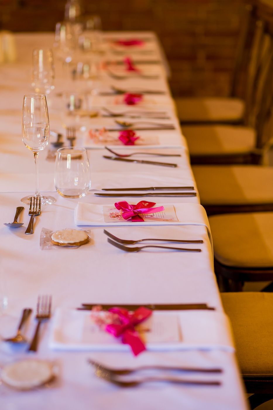 Formal place settings with pink flower petals along white tablecloth at wedding reception.