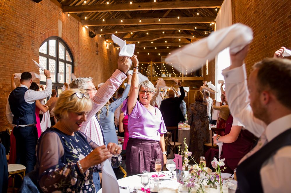 Wedding reception guests dining in a warm-lit brick venue with string lights and elegant table settings.
